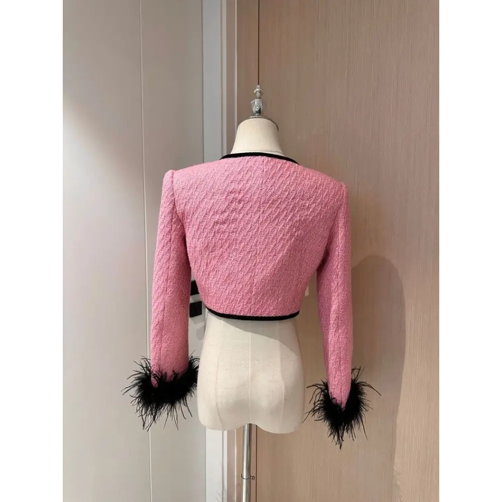 Pink tweed jacket with black trim and feathered cuffs.