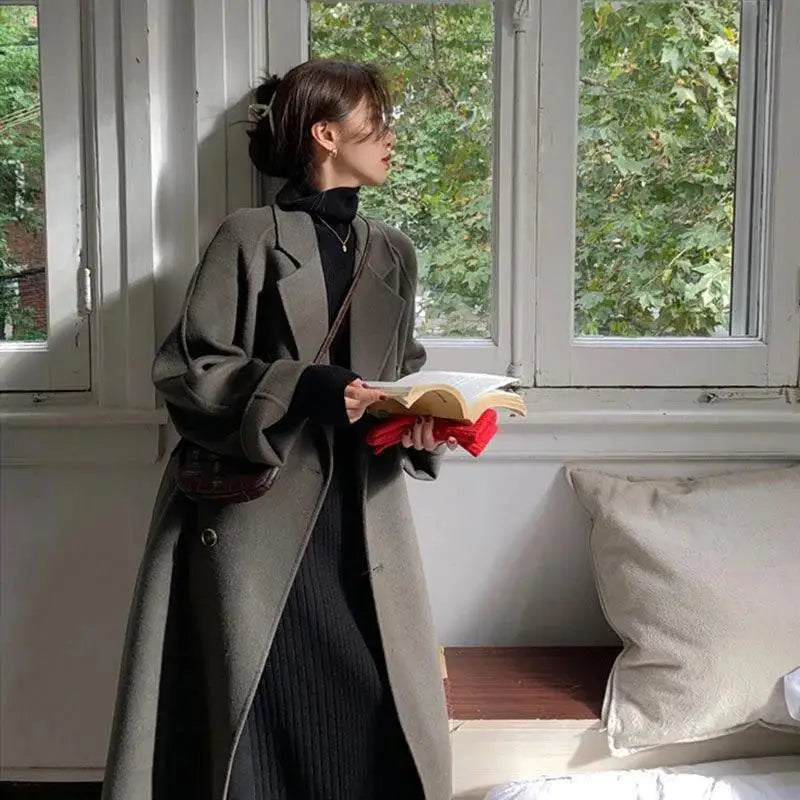 Woman in a long gray coat holding a book.