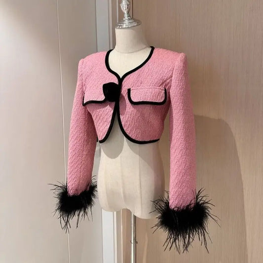 Pink tweed jacket with black trim and feather cuffs.